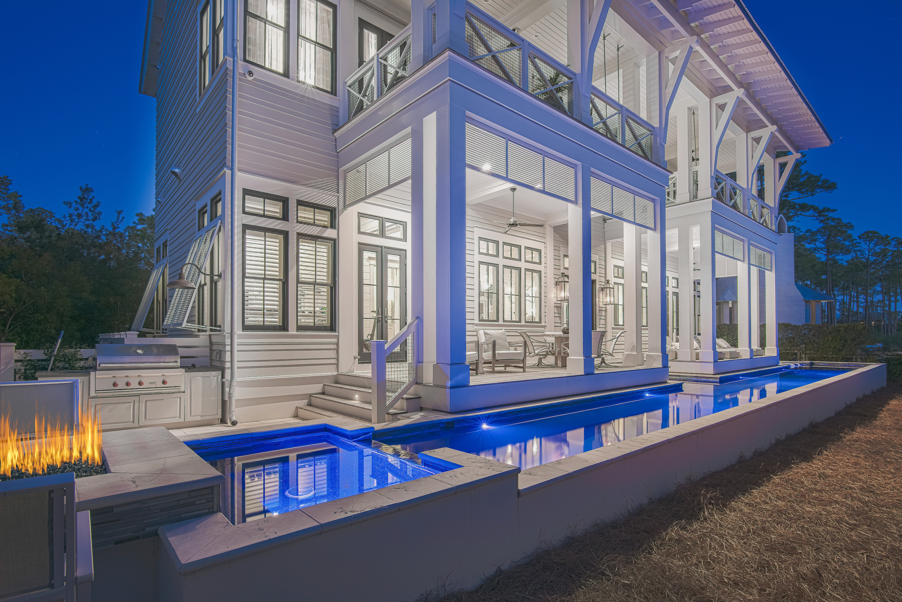 A evening view of a fully lit luxury Watercolor home featuring it's private pool with colored lights