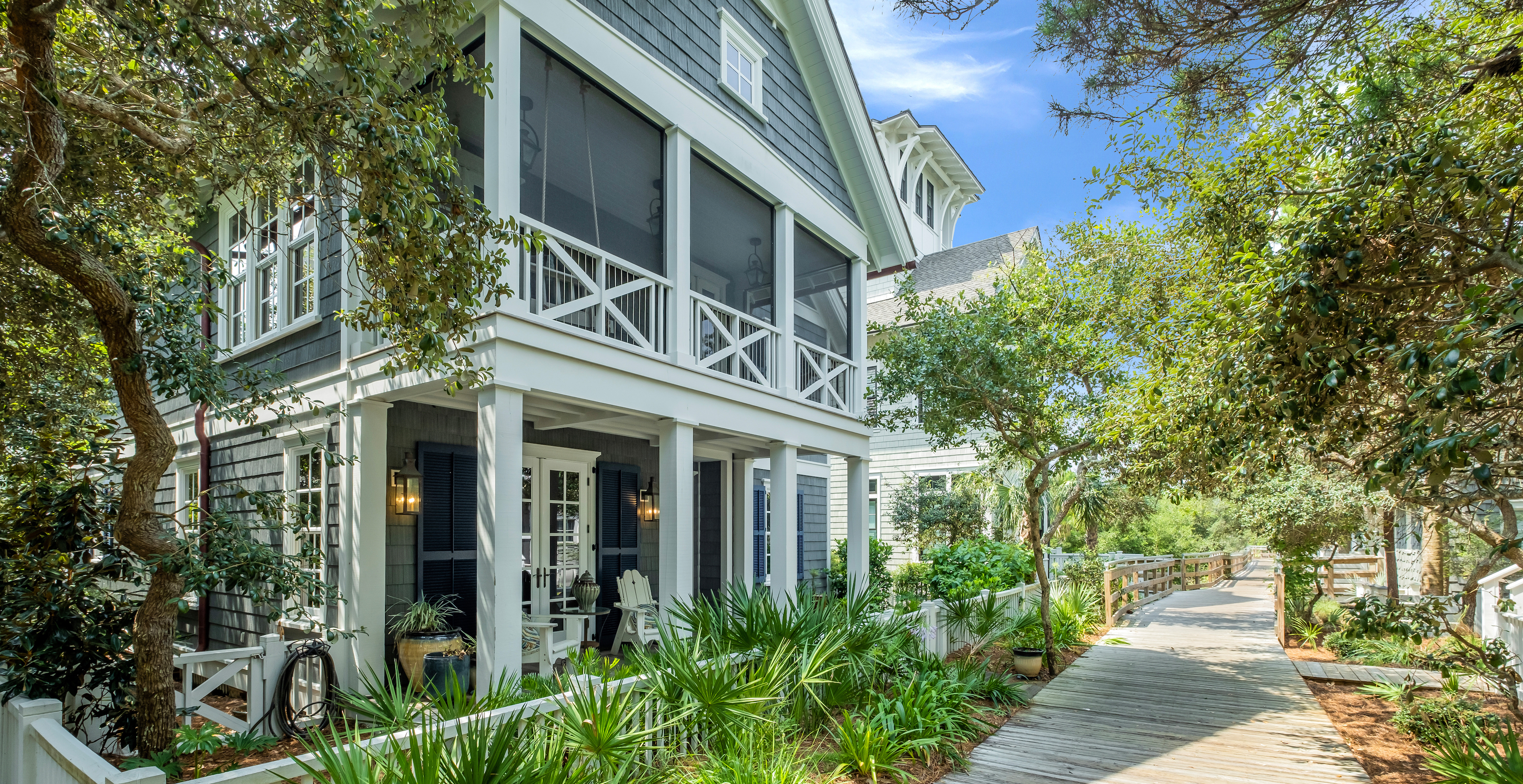 A 2 story Watersound beach cottage in front of a community walking path lined by palmettos