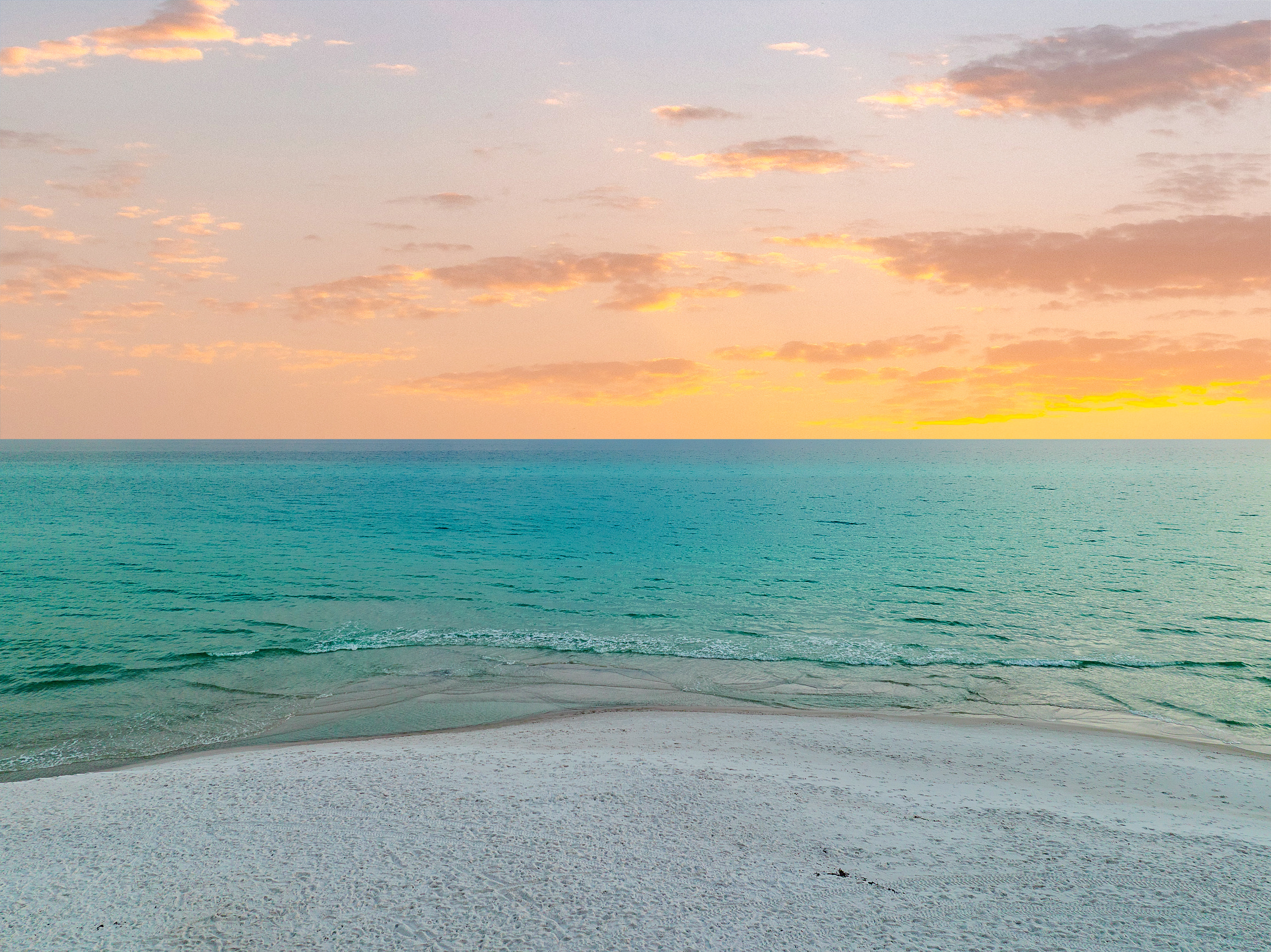 A serene sunset photo of the beach with white sand and brilliant blue gulf water