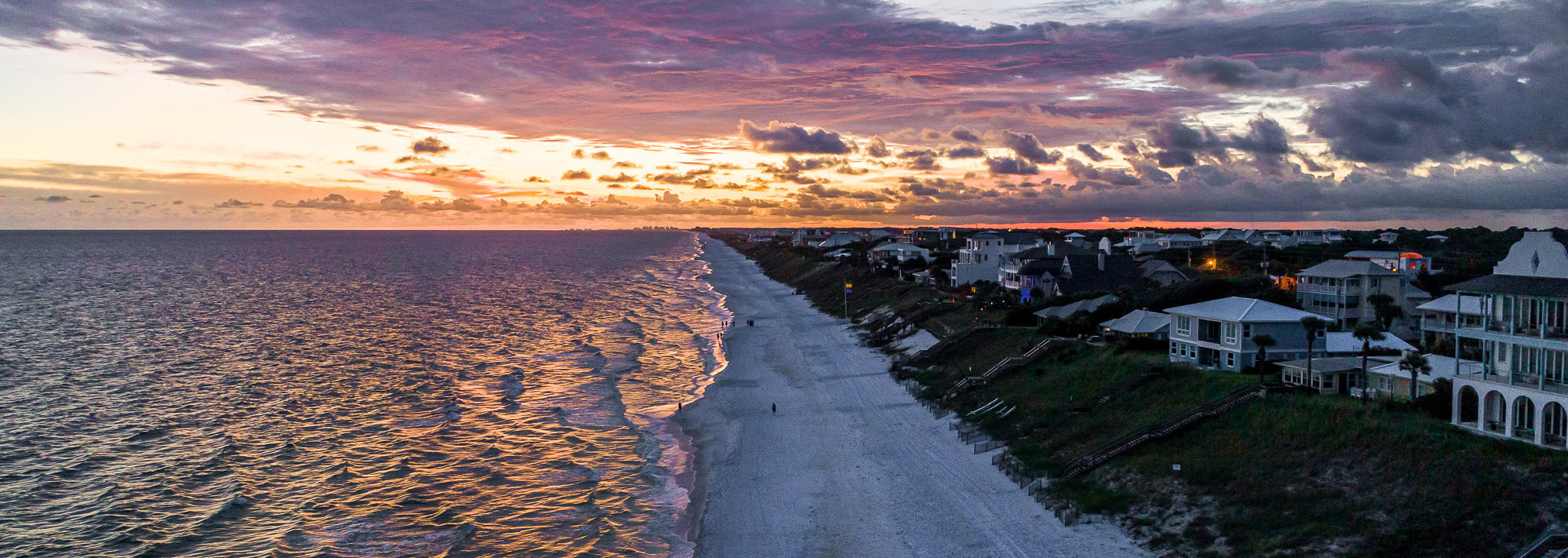 Sunset over Seagrove Beach with people having a bonfire on the sand at the shoreline.